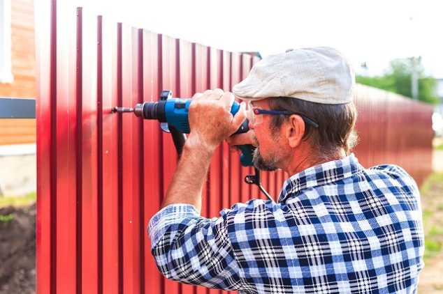 Man drilling a screw into a fence